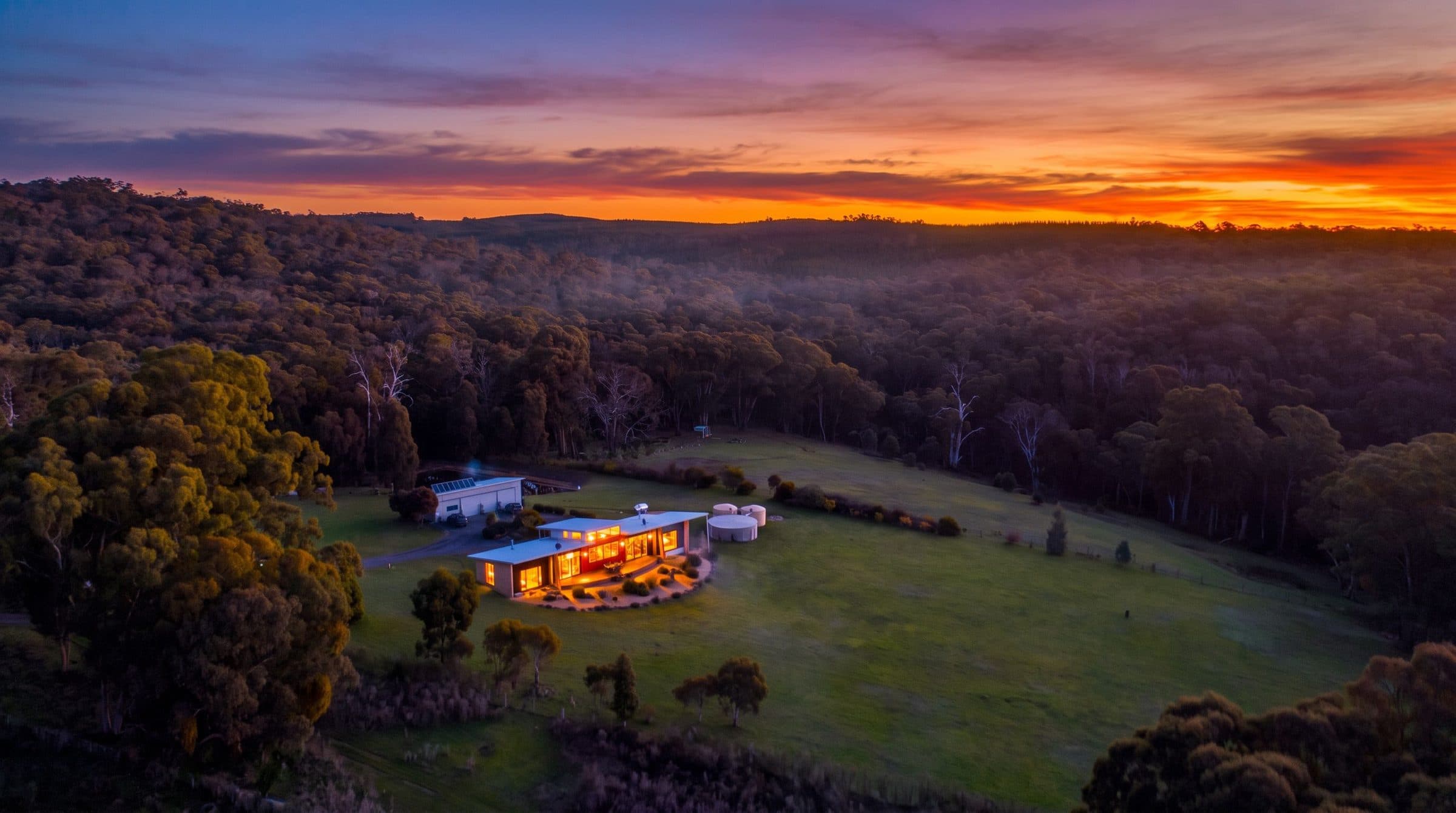 Arinya Retreat lit at dusk, seen from the air across the bushland